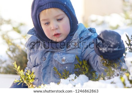 Cute caucasian liittle boy with bright blue eyes in winter clothes and hat (hood) on winter background. Healthy childhood. Outdoors, winter activity. Copy space, close up portrait. 