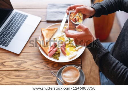 Blogger takes pictures of the Breakfast on the smartphone. Concept of creating content for social networks. Focus on the phone screen. Laptop and eat on the table.. American style breakfast.