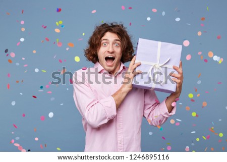 Joy, great fun, happiness, portrait of a birthday man received a gift box, happy photographed around falling confetti on a blue background. The man was congratulated handed a gift, he delighted.