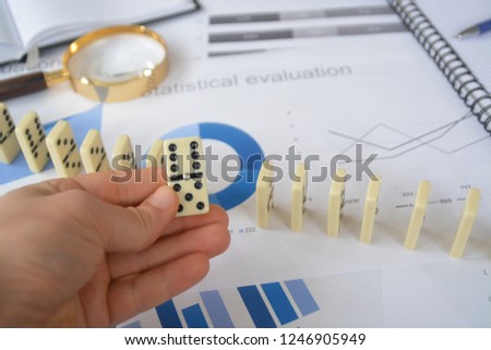 Holding a domino in front of a table full of statistics and a magnifying glass - concept for building blocks in a business context or to select the right person to drive a concept forward