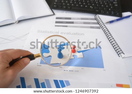 A young man is holding a magnifying glass in his hand, looking at statistic figures - a business concept on the subject of sampling and selecting the right target group and examining it Royalty-Free Stock Photo #1246907392