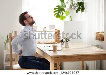 Tired millennial office worker stretch in chair suffer from sitting long in incorrect posture, male employee have back pain or spinal spasm working in uncomfortable position. Sedentary life concept Royalty-Free Stock Photo #1246921087