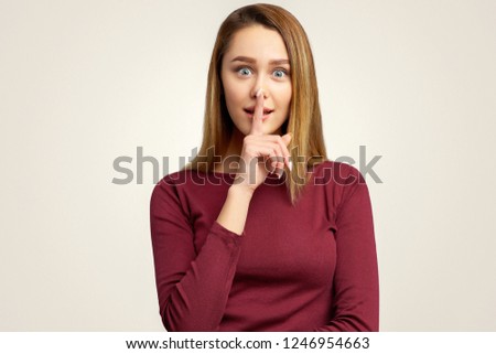 A mysterious sweet girl makes a gesture quietly, holding index finger on lips.  The woman mysteriously tells the secret to her best friend, gossips about guys, asks to keep secret and remain silent.