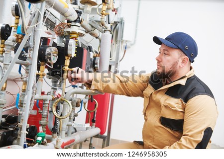 heating engineer or plumber inspector in boiler room taking readouts or adjusting meter Royalty-Free Stock Photo #1246958305