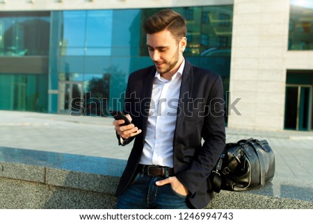 Young urban professional man using smart phone. Businessman holding mobile smartphone using app texting sms message wearing jacket With office buildings on the background