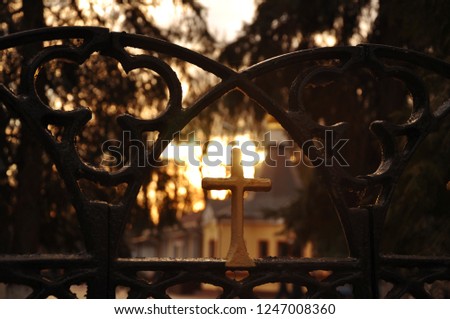 A small cross on the fence in the sun light and the church and trees in the background. Central Park, Gomel, Belarus.