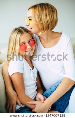 Funny mother and daughter in colorful sunglasses have a fun and hugging on the couch at home