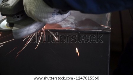 Metal polishing with a hand sander with a polishing disk. Clip. Factory worker at workshop grinding steel rod with abrasive disc and flying sparks. Hand grinder workflow creation stainless pipe