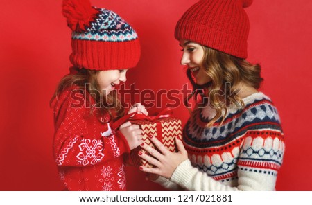 happy family mother and child daughter with christmas gifts and hats on red background