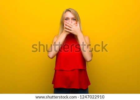 Young girl with red dress over yellow wall covering mouth with hands for saying something inappropriate