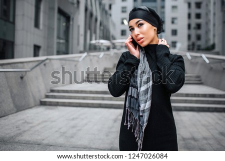 Picture of arabian model talking on phone. She looks to left and hold one hand on neck.