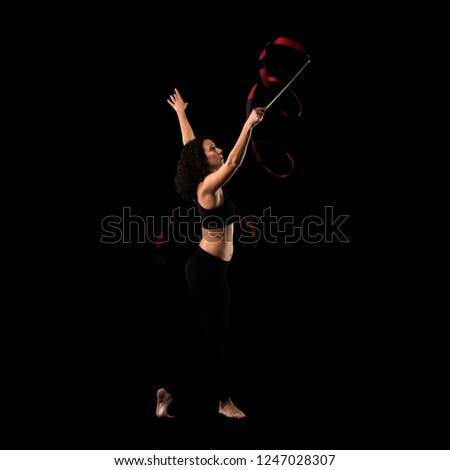 Woman doing rhythmic gymnastics with ribbon on black background