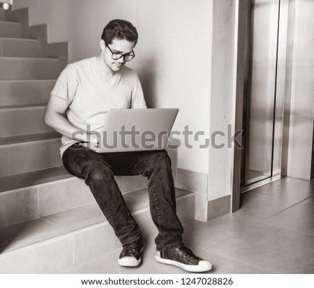 Handsome young freelancer man using laptop computer sitting at stairs inside the building. Freelance work, Business people concept . Image in black and white color style