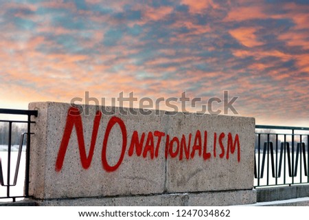 Red inscription with slogan "No nationalism" on the concrete fence of the city embankment against a dramatic sky. Inscription protest against racial discrimination.