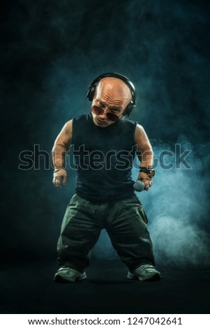 Portrait of stylish midget MC in with headphones and sunglasses posing with microphone. Royalty-Free Stock Photo #1247042641