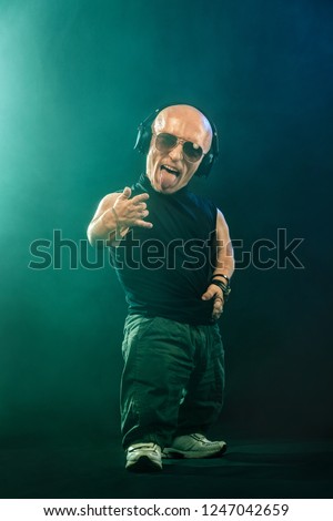 Portrait of stylish midget MC in with headphones and sunglasses posing with microphone. Royalty-Free Stock Photo #1247042659