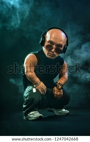 Portrait of stylish midget MC in with headphones and sunglasses posing with microphone. Royalty-Free Stock Photo #1247042668