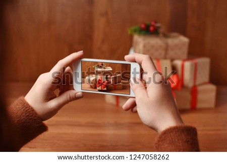 A girl taking photo of pile of presents on wooden table with her phone