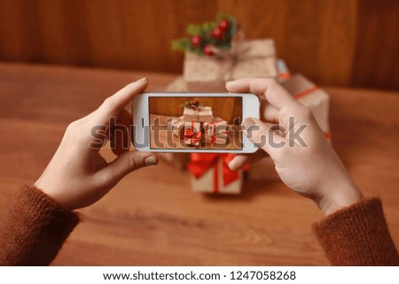 A girl with phone taking a photo of presents on wooden table