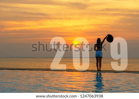 Lifestyle woman Happy New Year Card 2019.  Silhouette woman relaxing and freedom on the swimming pool near the sea and beach in the sunset as part of Number 2019.  Summer and Holiday Concept