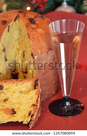 a panettone cut into slices ready to eat, in the background Christmas decorations. in the foreground a glass full of sparkling wine