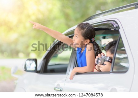 Happy girl is pointing fingers and boy take picture with vintage camera from window car, travel concept