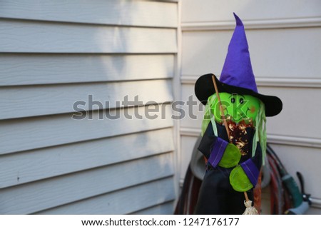 Green Felt Witch Halloween Decoration with Black Eyes Wood Broom Blue Cape and Hat with Shiny Bronze Ruffles against White Wall of Victorian-Style Townhome in Burke, Virginia
