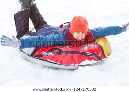 Happy teenage boy sliding down hill on snow tube laughing and showing excitement while he slides downhill.  Snow tubing on winter day outdoors. Winter activity, leisure and entertainment concept