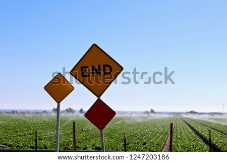 End sign with farmers field being watered by sprinklers in the background in Southern California showing climate change and irrigation possibilities in an arid land.
