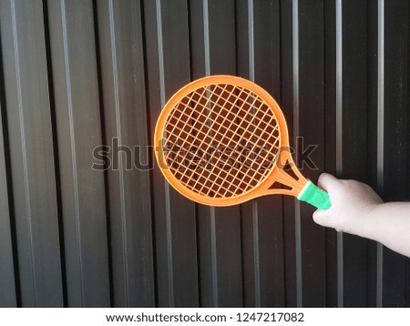 Boy holding a wooden badminton toy on a brown backdrop.