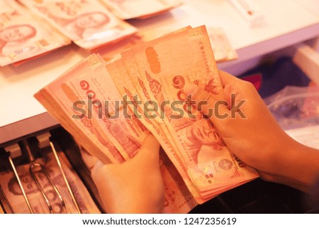 Women's hand counting money, red banknotes. Price 100 baht in the store, in the front.