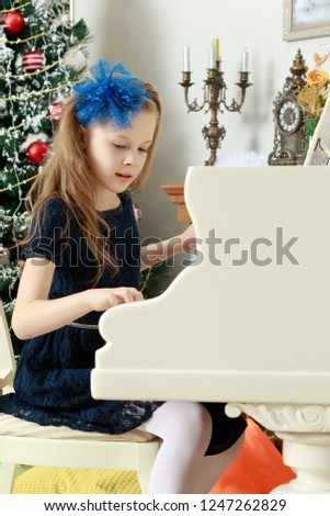 Beautiful, elegant little girl holding hands on the keys of a white Grand piano. Girl playing at the Christmas concert in the music school.