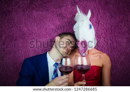 Portrait of unusual couple on purple background. Freaky young woman in comical mask drinking wine with guy in suit. Young man with girl unicorn. Royalty-Free Stock Photo #1247286685