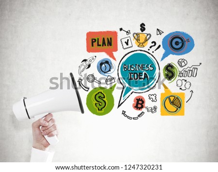 Hand of unrecognizable businessman in white shirt holding megaphone near concrete wall with colorful business idea drawing.