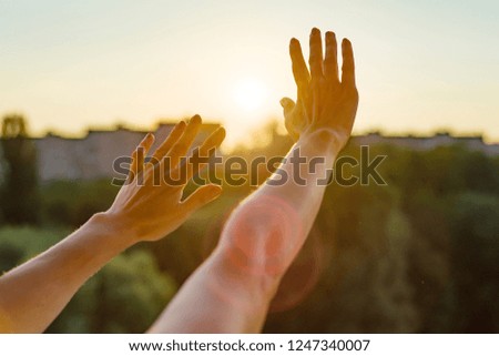 Hands open to the sunset, meditation, religion, prayer, background of the open window in the house, the silhouette of the city and the evening sun.