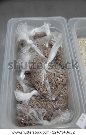 Storing buckwheat noodles in a plastic box and cellophane package for cooking Asian food Wok, against the background of a stainless steel table in the restaurant’s kitchen.