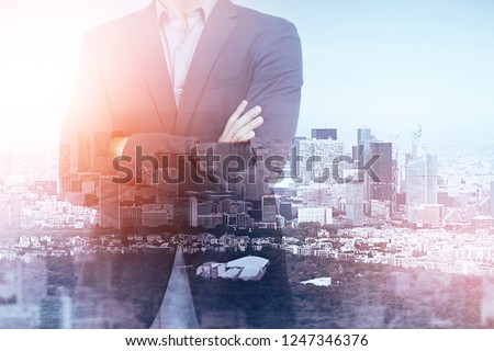 Unrecognizable businessman standing with crossed arms over modern cityscape background. Concept of business success. Toned image double exposure