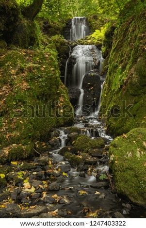 Stunning tall waterfall flowing over lush green landscape foliage in early Autumn