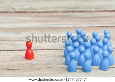 a crowd of blue pawns, one red pawn in the middle, on a wood table. grey background, studioshot.
