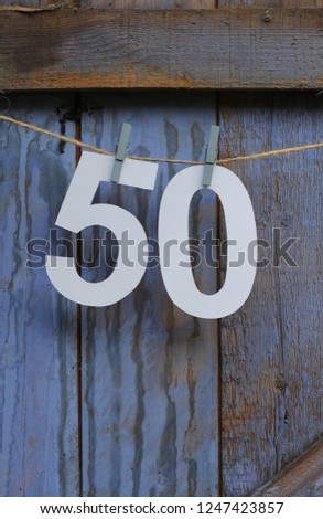 A paper cut number fifty pegged to string in front of a blue painted wooden barn door, a rustic , unusual bunting for a fiftieth  birthday or anniversary 