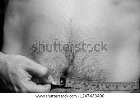 A man measuring his waist size with a measuring tape. This image can be used to represent dieting or weight loss. 