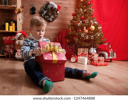 Christmas miracle. Child boy opens magic gift box. Happy and surprised children in xmas night. Little hipster in red Santa hat with finger pointed up. Child with Christmas gift.