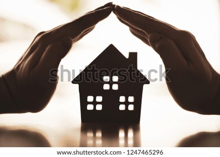 Hands of a young woman surround a wood house model. Real estate agent offer house, property insurance and security, affordable housing concepts