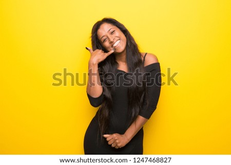 Young afro american woman on vibrant yellow background making phone gesture. Call me back sign