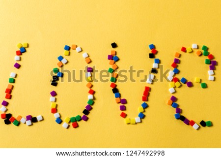 The word love drawn with multicolored small mosaic on yellow background.