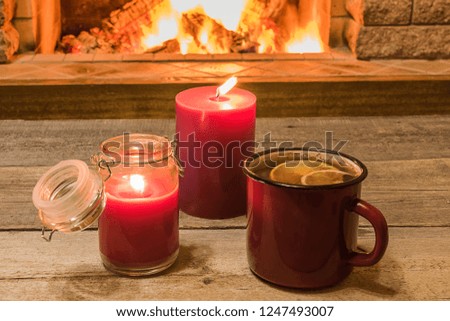 Cozy scene against fireplace with red enameled mug with tea, and two candles.
