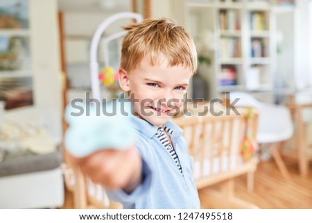 Blond boy is having fun in the nursery with baby bed in the background