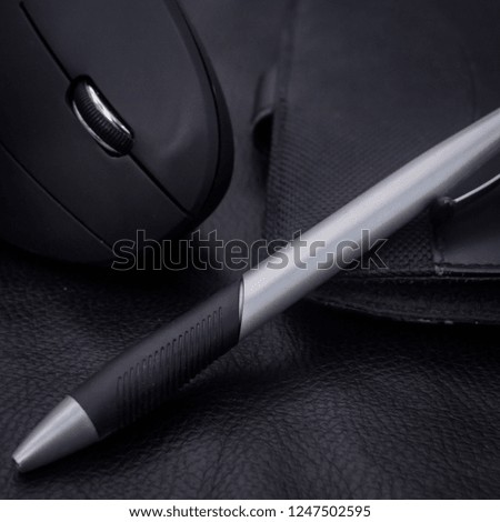 Soft blur of a black wireless and elegant mouse, silver pen and leather agenda, on a black background