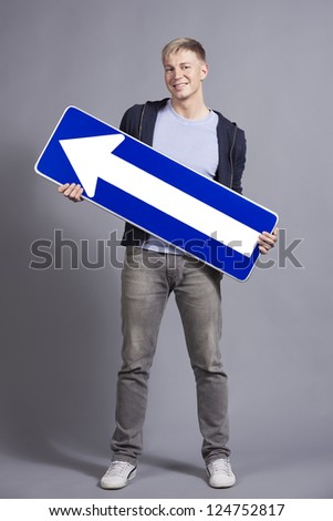 Smiling friendly man holding direction arrow sign pointing upwards with space for text isolated on grey background.