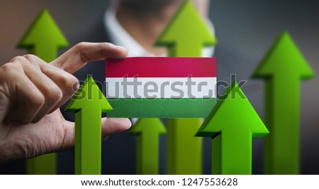 Nation Growth Concept, Green Up Arrows - Businessman Holding Card of Hungary Flag 